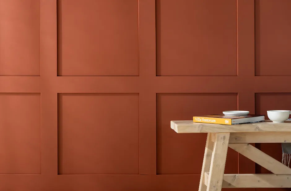 Burnt orange coloured wall with shaker style panelling. Wooden bench in corner